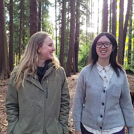 Cassandra and Juanita, in the forested area by Lower Mall Research Station. Two people walking side-by-side in a forested area.
